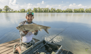 What is a Grass Carp - Man holding grass carp with lake in background