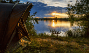 What is Specimen Carp Fishing - Camping gear and carp rods beside a lake with sunset