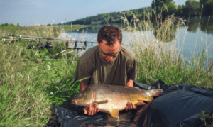 Most Common Mistakes Made While Carp Fishing - angler picking up carp on unhooking mat